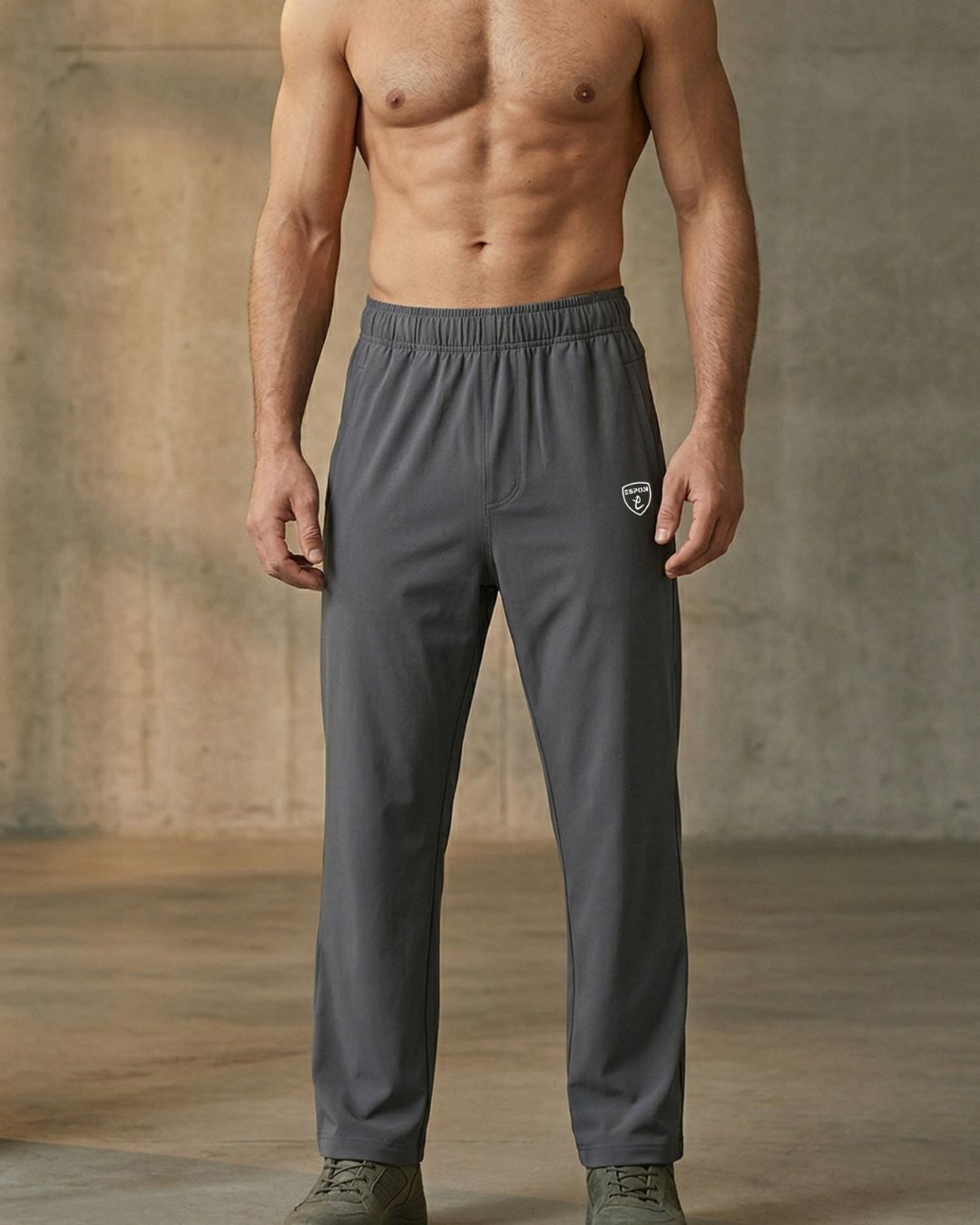 Athletic man modeling gray track pants with elastic waist in a minimal indoor setting