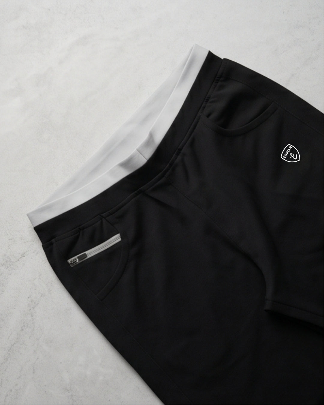 Black track pants with white waistband, side zipper pocket, and activewear logo on marble background
