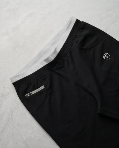 Black track pants with white waistband, side zipper pocket, and activewear logo on marble background