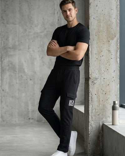 Man in black track pants with cargo pockets and black t-shirt, posing in modern indoor space