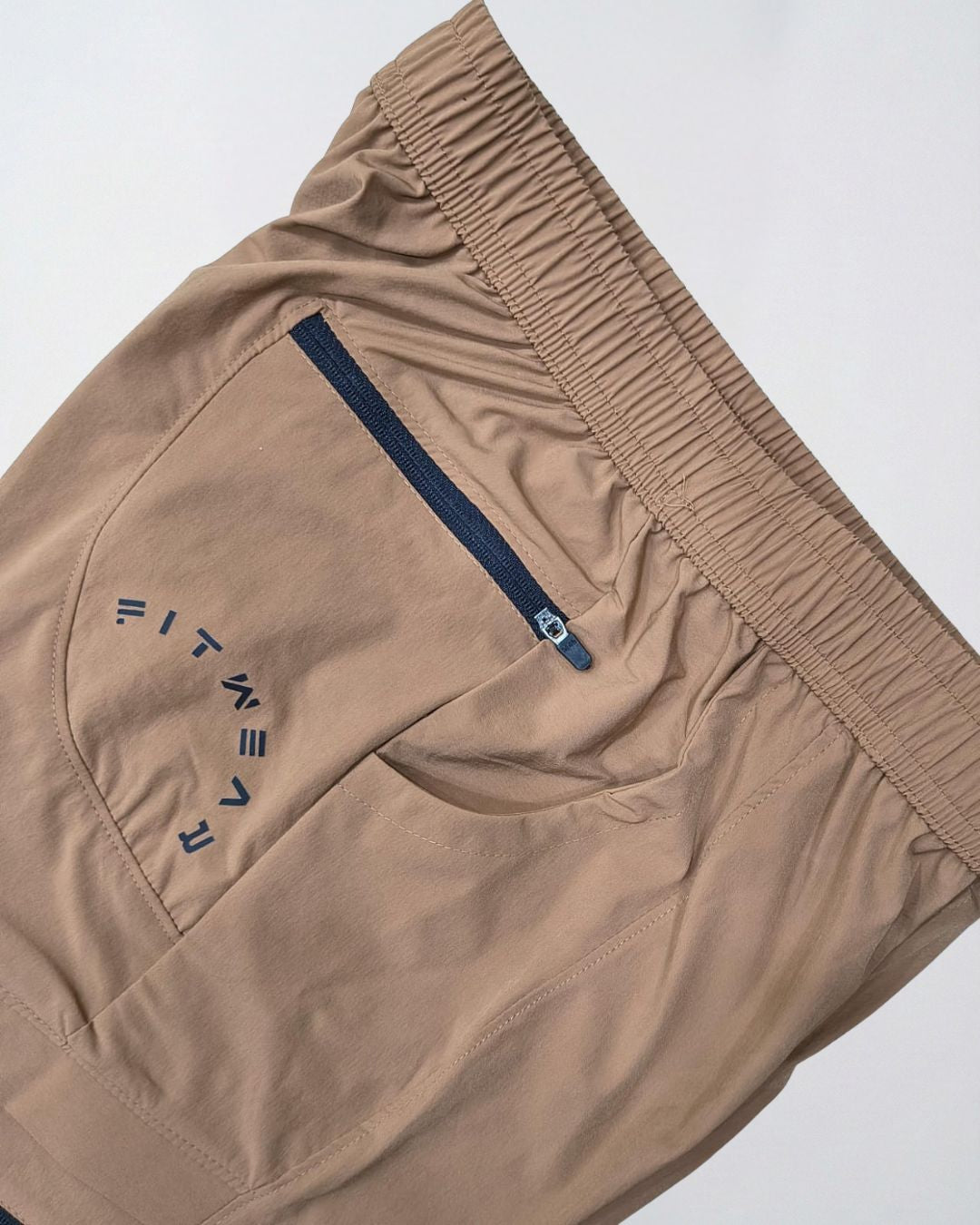 Beige track pants with elastic waistband, zip pocket, and sporty graphic detail
