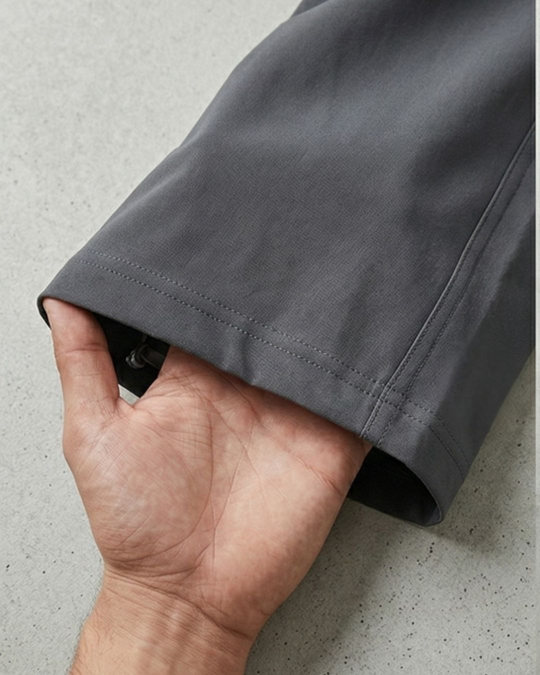 Close-up of a hand holding the hem of grey track pants on a concrete surface