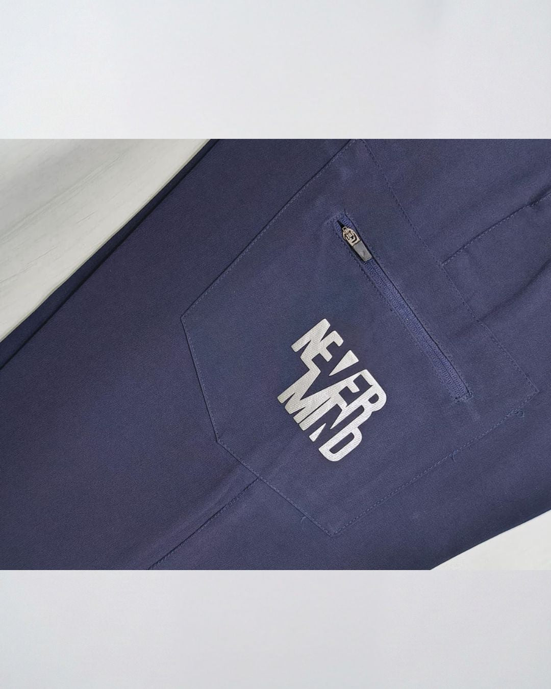 Navy blue track pants with zippered pocket and 'NEVER MIND' text, activewear closeup