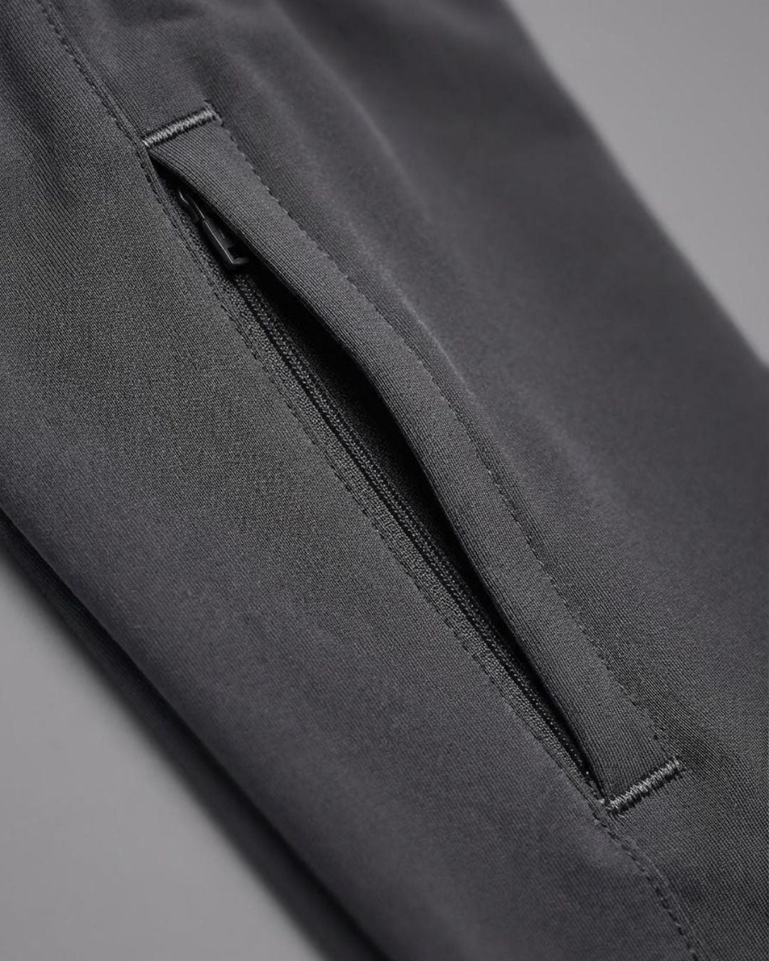 Close-up of black track pants with a zippered side pocket on gray background