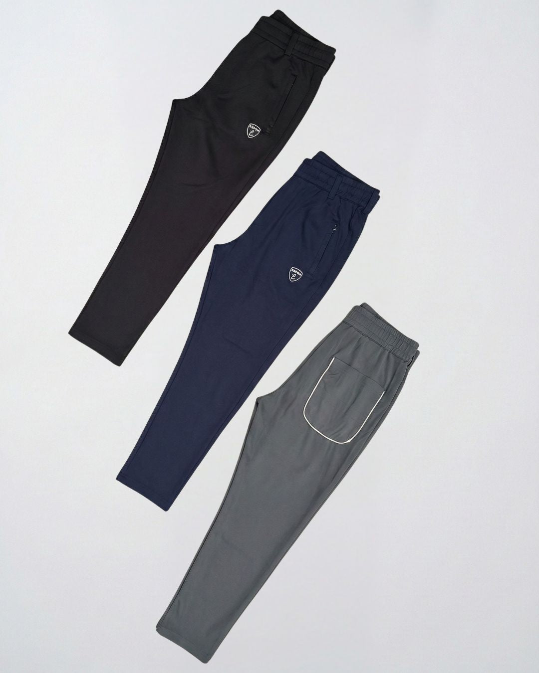 Three athletic track pants in black, navy, and grey colors displayed flat on a light background.
