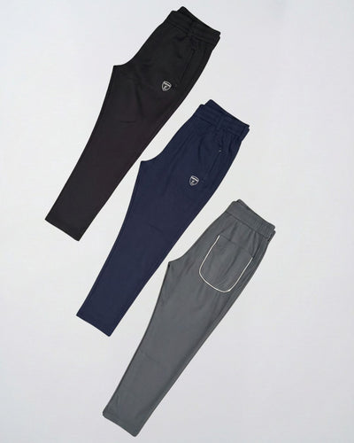 Three athletic track pants in black, navy, and grey colors displayed flat on a light background.