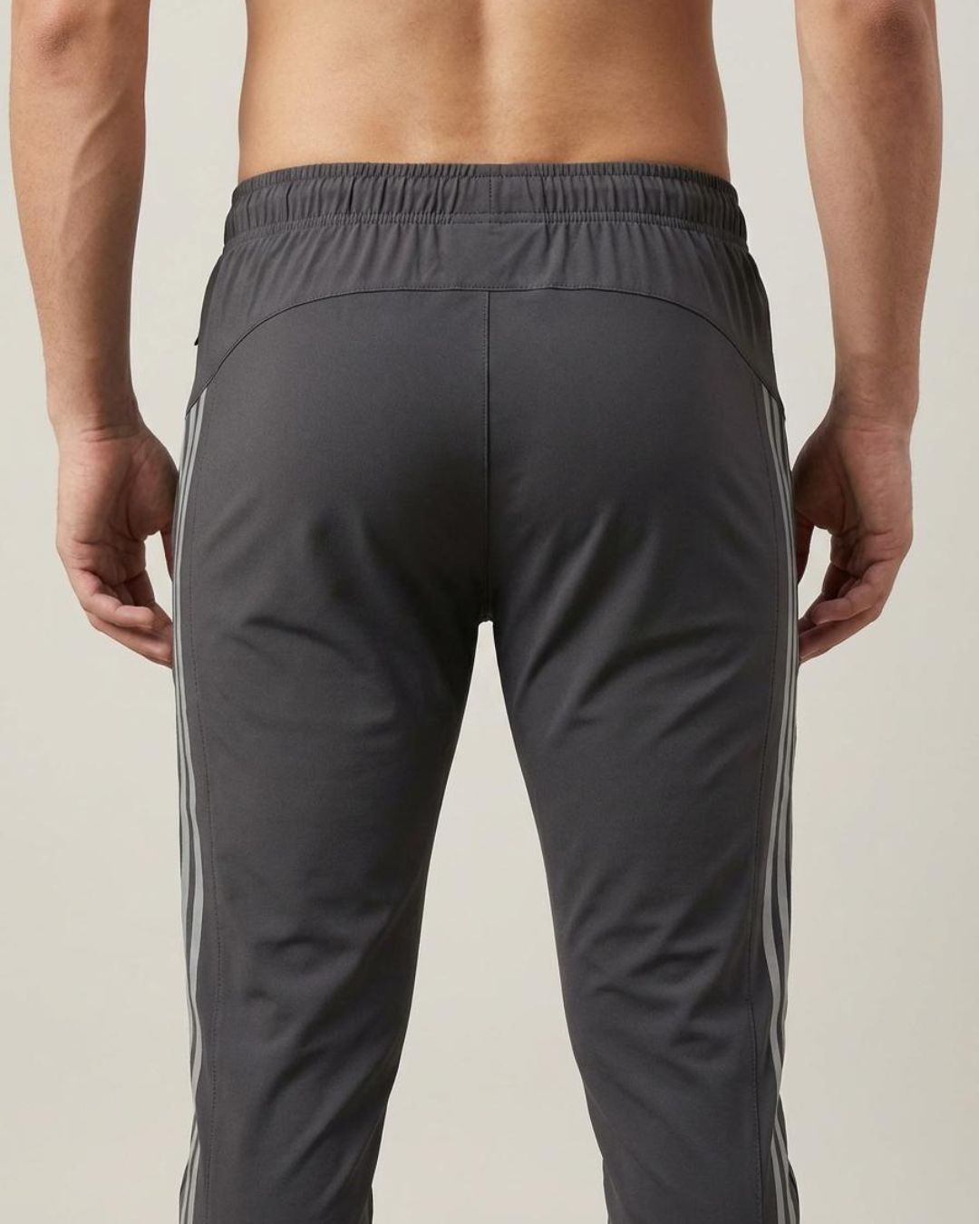 Back view of a man wearing dark grey track pants with side stripes and elastic waistband