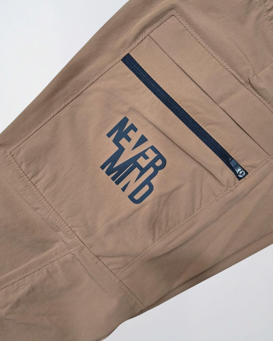 Beige track pant with zippered pocket and 'NEVER MIND' text print, activewear detail.