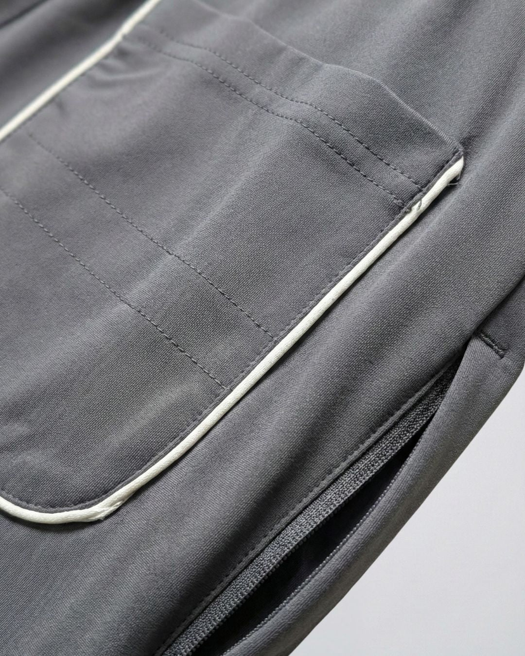 Close-up of grey track pants pocket with white piping and zipper, activewear fabric