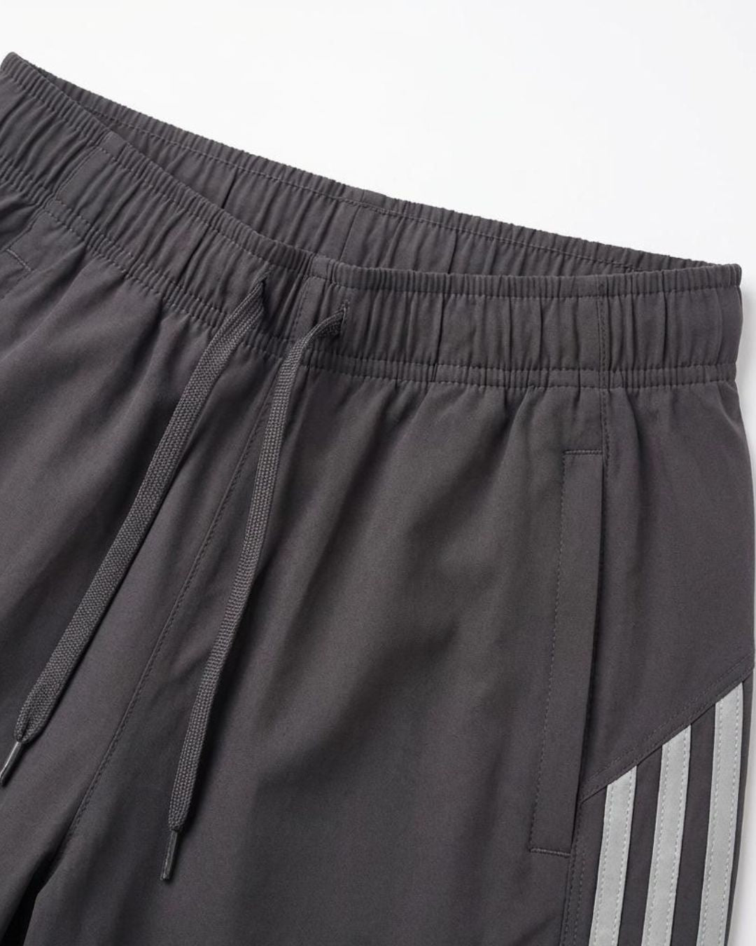 Dark grey track pants with elastic waistband, drawstring, side pockets, and reflective stripes