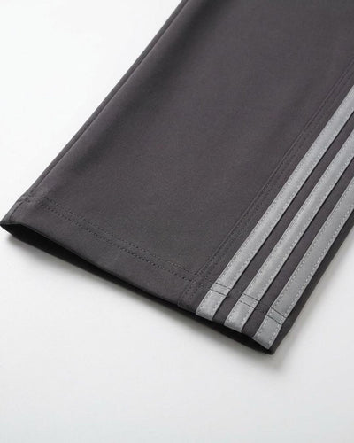 Close-up of grey track pant hem with three reflective side stripes on white background