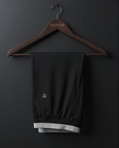 Black track pants with white trim on wooden hanger against dark background, activewear display